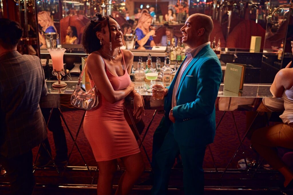 A Black mand and woman laugh while standing at a cocktail bar