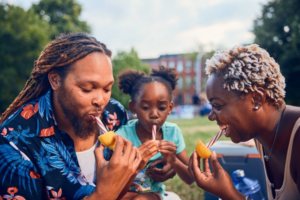 A man, woman and child suck on lemon sticks in the park