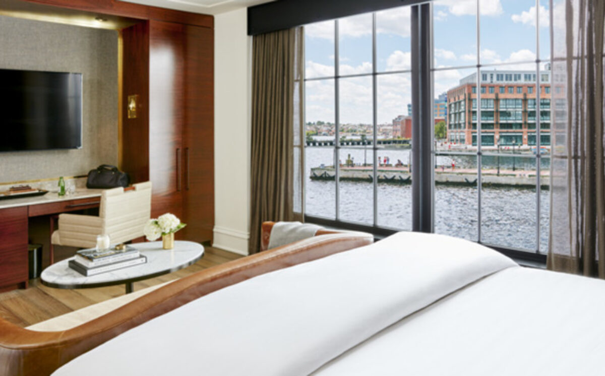 Hotel room with a bed, couch, and desk. With view of harbor from the window